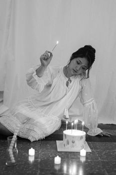 Woman celebrating birthday with candlelit cake in soft black and white setting.