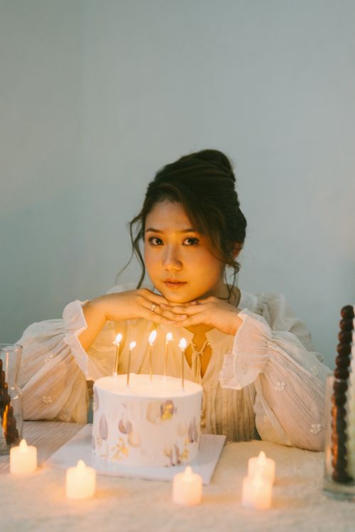 Free A young woman enjoys a cozy birthday celebration with a candle-lit cake at home. Stock Photo