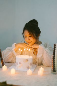 A young woman in a serene setting admires a candlelit birthday cake, creating a warm and festive atmosphere.