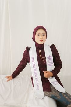 Young woman in hijab celebrates graduation with elegant attire and sash indoors. - Fotografer Sidoarjo