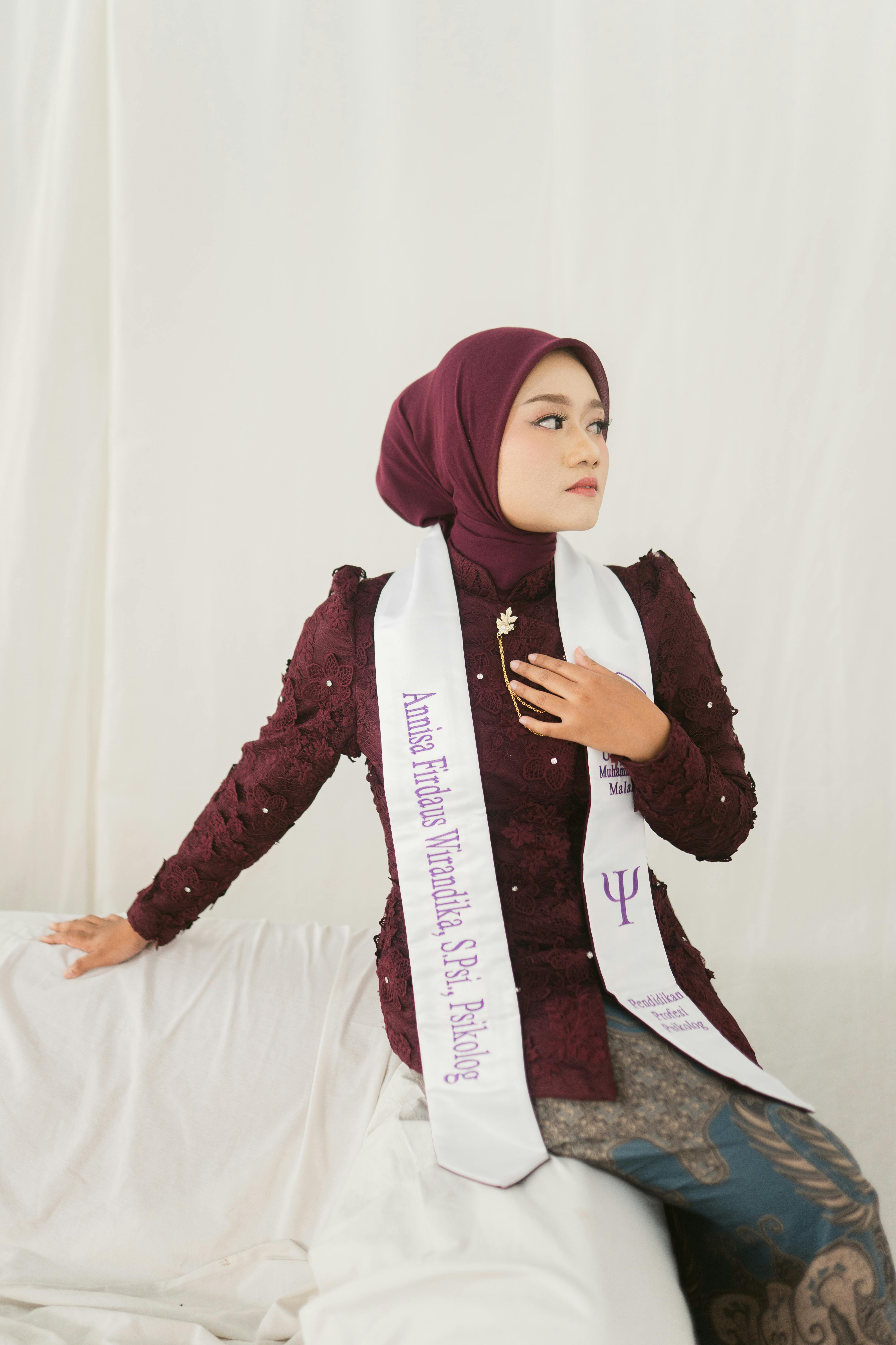 Young woman in graduation attire poses elegantly against white backdrop.