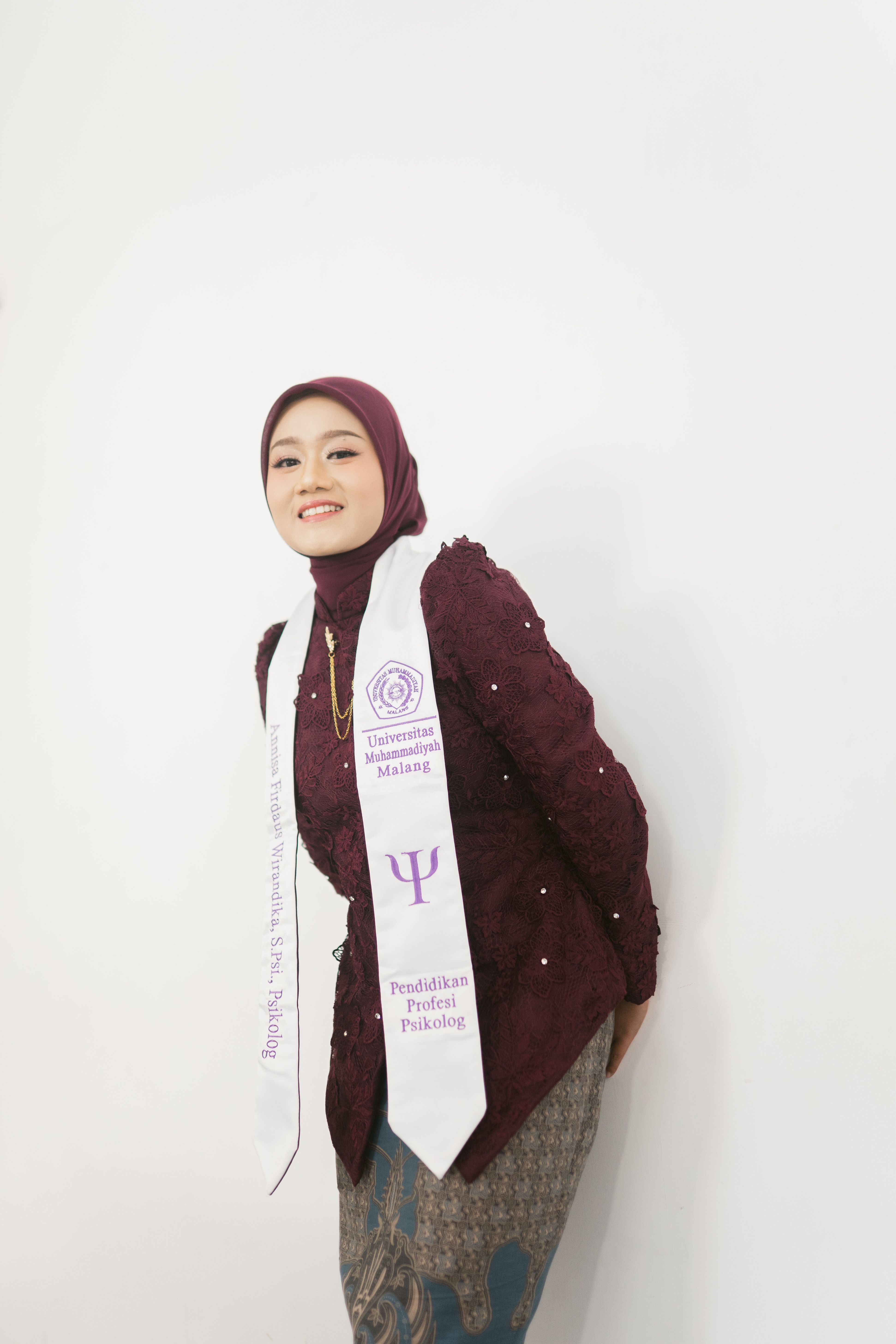 A young woman in traditional attire poses with a graduation stole against a white background.