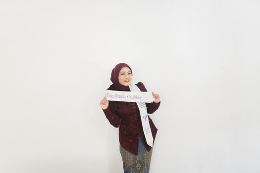 Young woman in a maroon outfit celebrating her graduation with a sash, smiling against a white background.