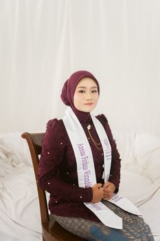 Elegant portrait of a young woman wearing a hijab and graduation stole, seated indoors. - Fotografer Sidoarjo