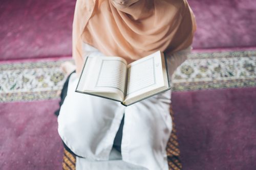 Free Young woman in peach hijab reading Quran indoors, exemplifying spiritual devotion. Stock Photo