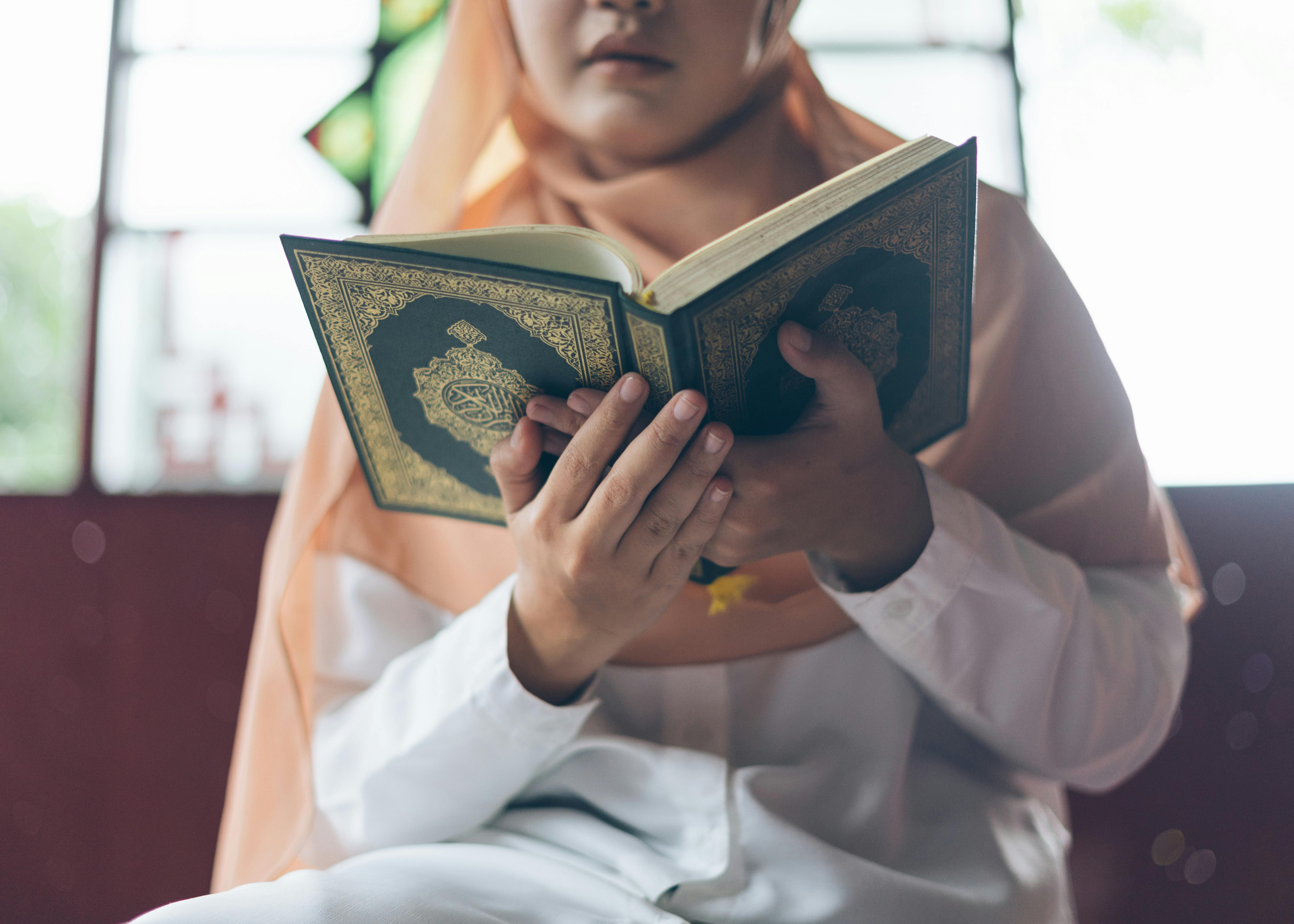 Bezpłatne Muzułmanka w hidżabie czyta Koran w pomieszczeniu zamkniętym, uchwytując w ten sposób duchową chwilę. Zdjęcie z galerii