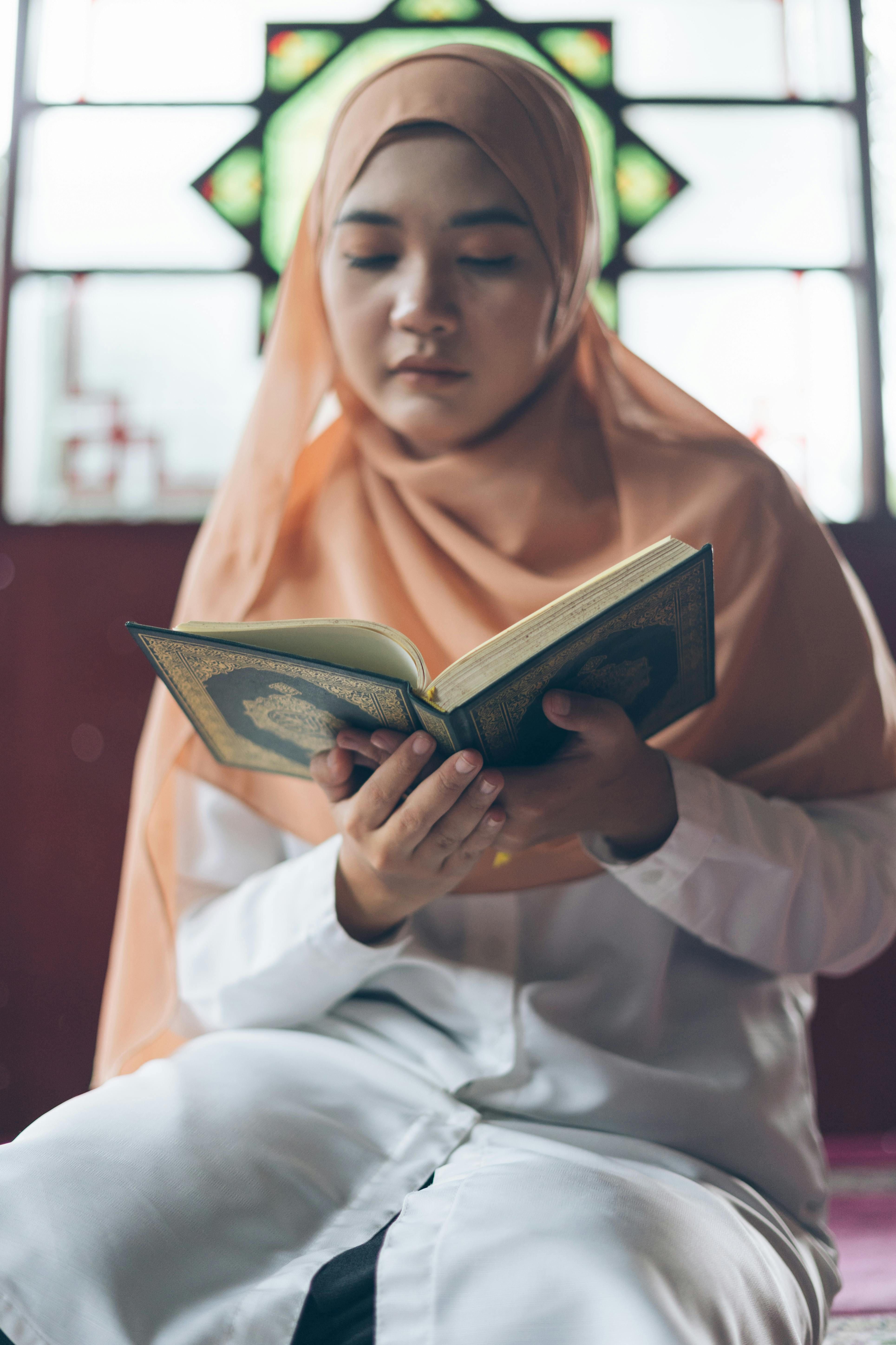 bezplatná Mladá žena v hidžábu čte svatou knihu uvnitř mešity, soustředěná a klidná. Základová fotografie