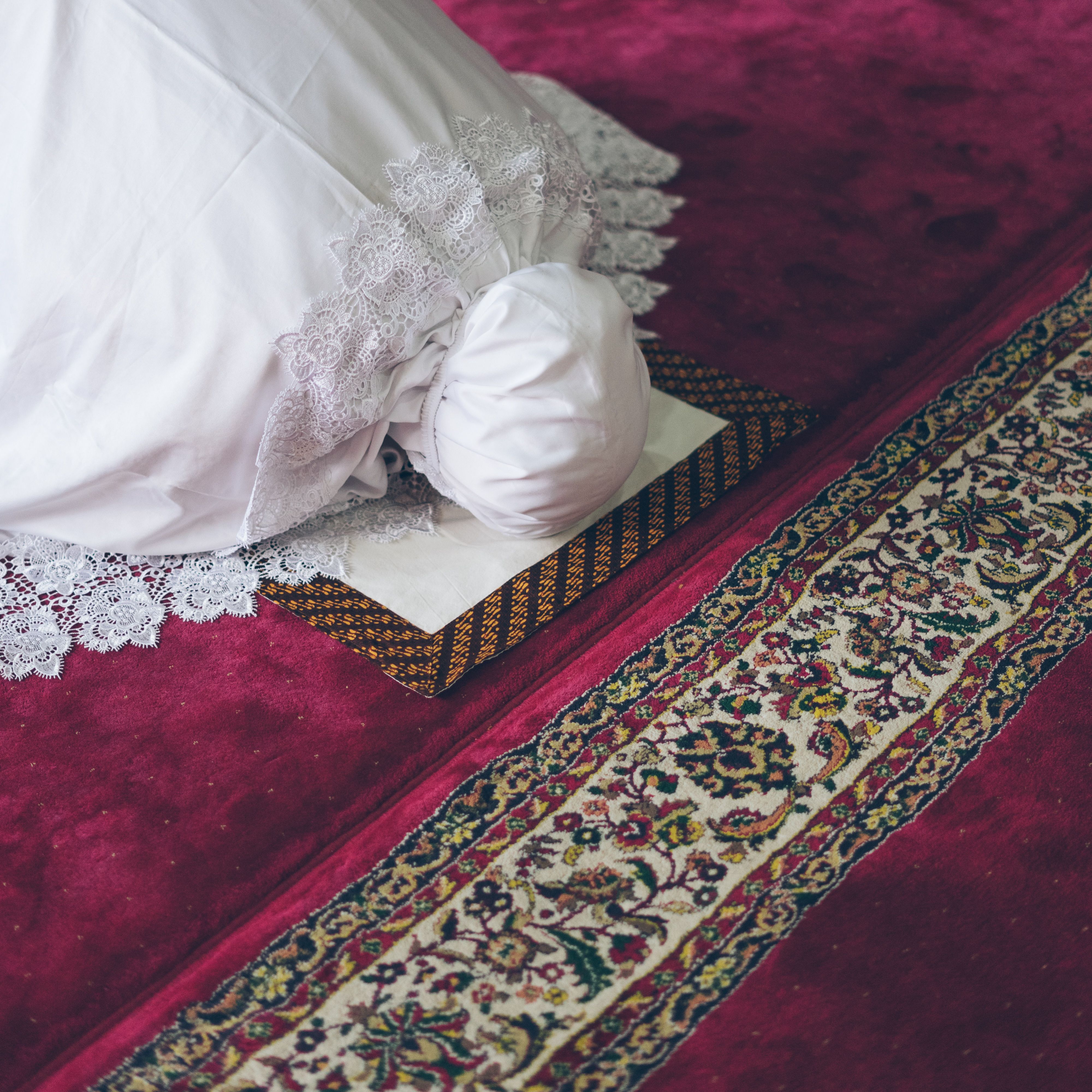 A woman in traditional attire performing prayer on a beautifully designed Persian carpet.