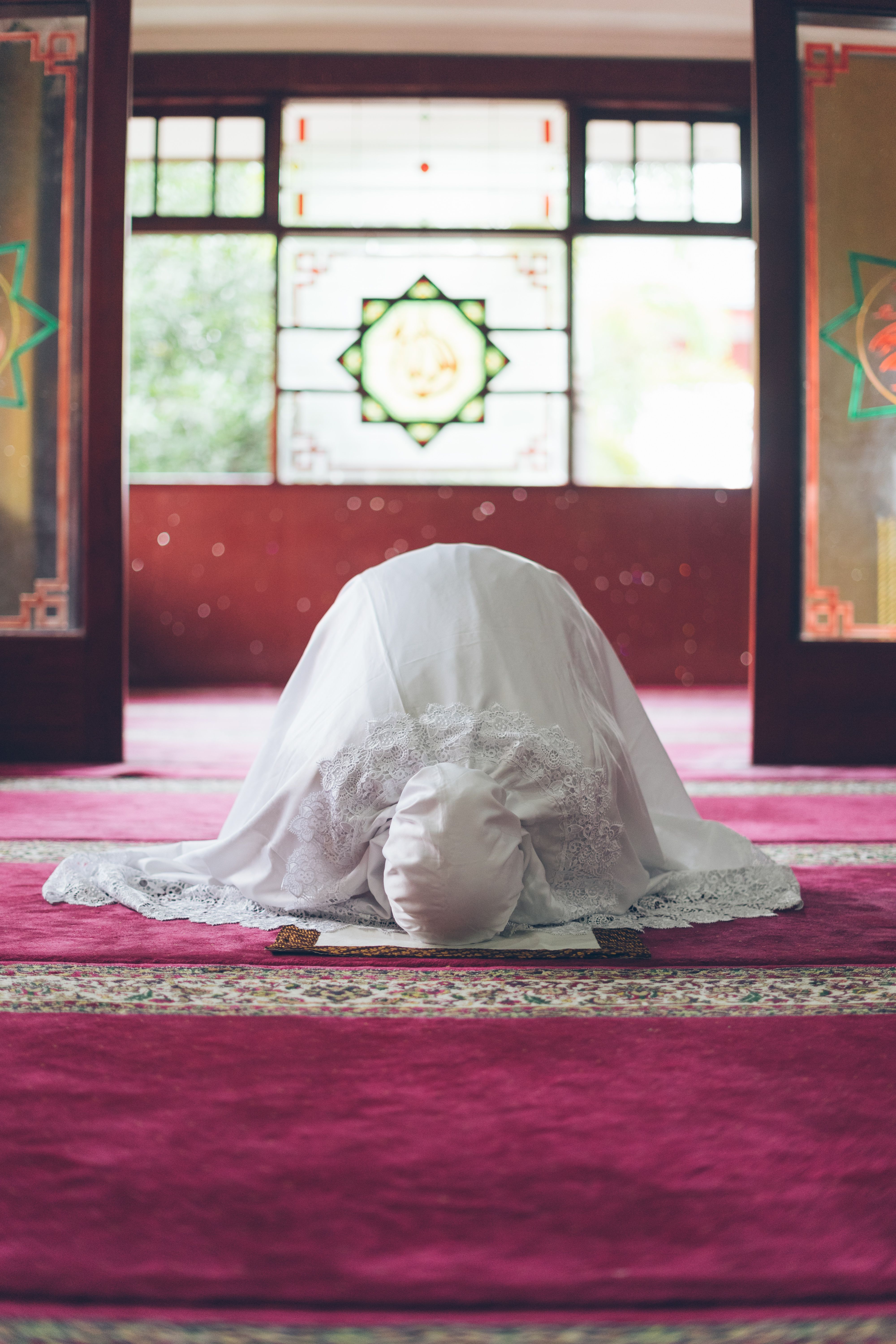 A woman in white attire prays inside a mosque, symbolizing devotion and spirituality.