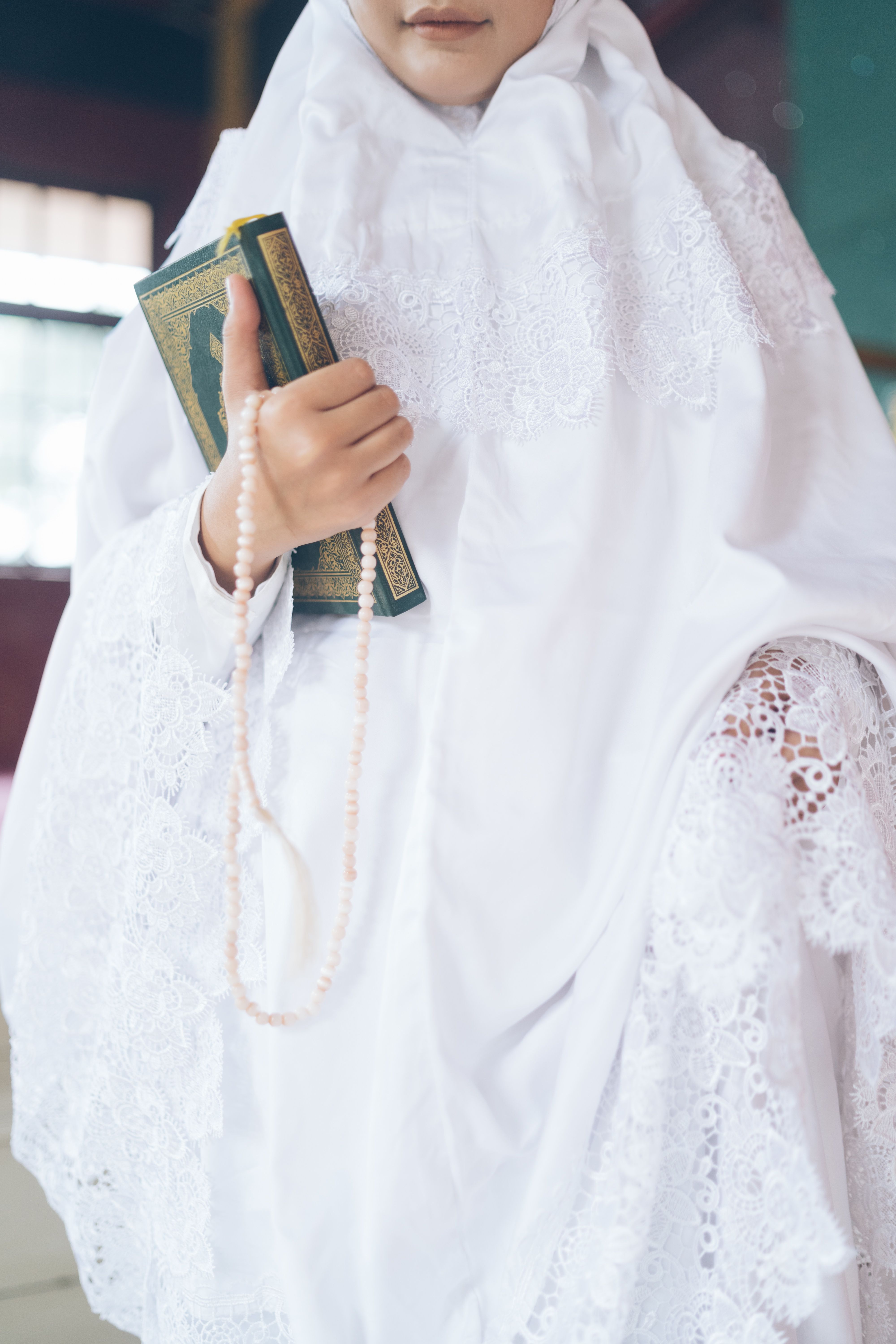A woman in a white robe holding a prayer book and a string of beads, symbolizing faith.
