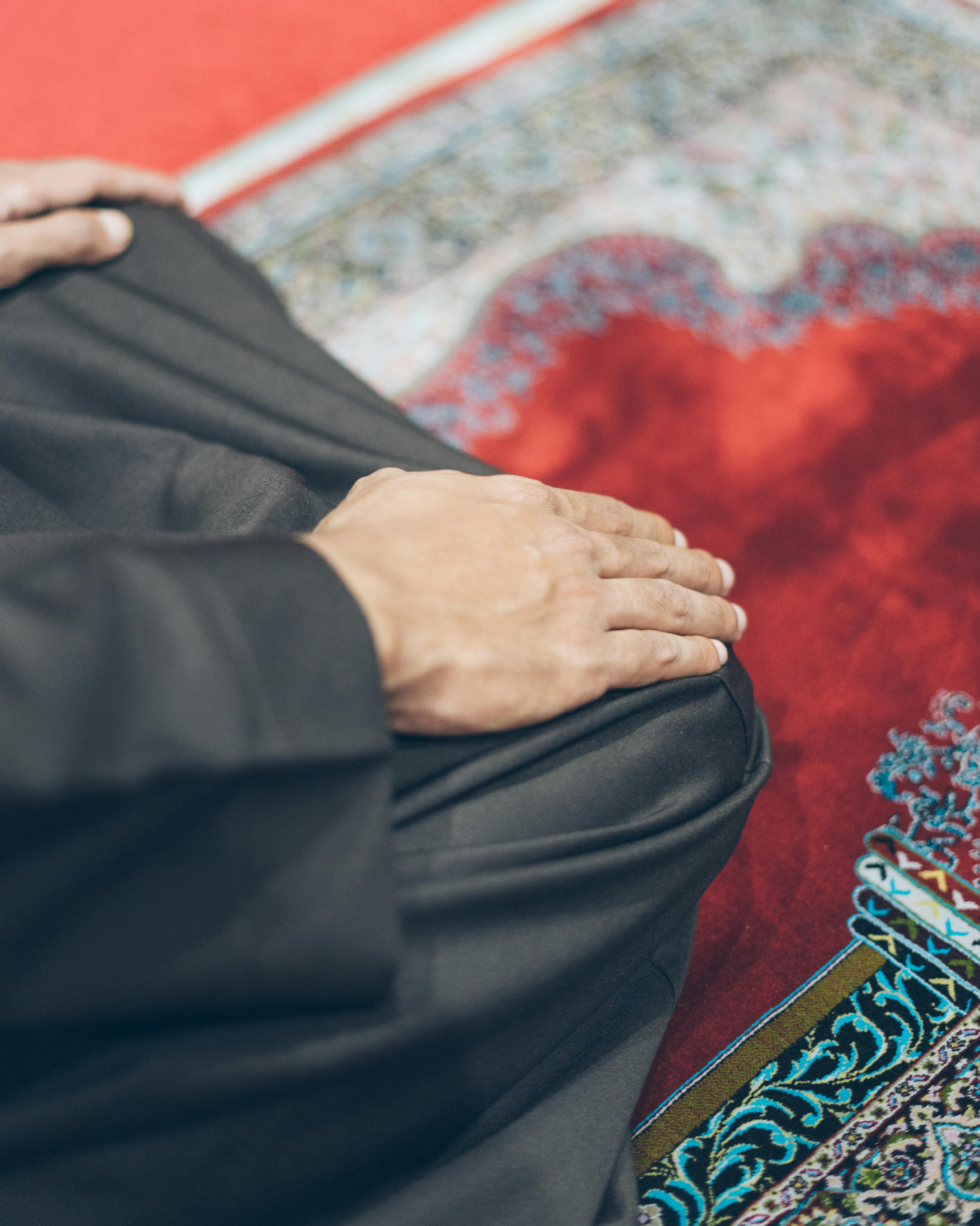 Close-up of hands resting on a patterned prayer rug in the posture of tashahhud during salah, illustrating the sitting position for dua after salatul tawbah