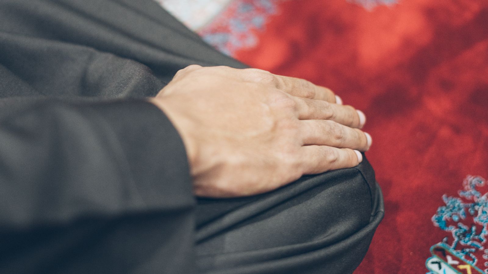Close-up of hands resting on a patterned prayer rug in the posture of tashahhud during salah, illustrating the sitting position for dua after salatul tawbah