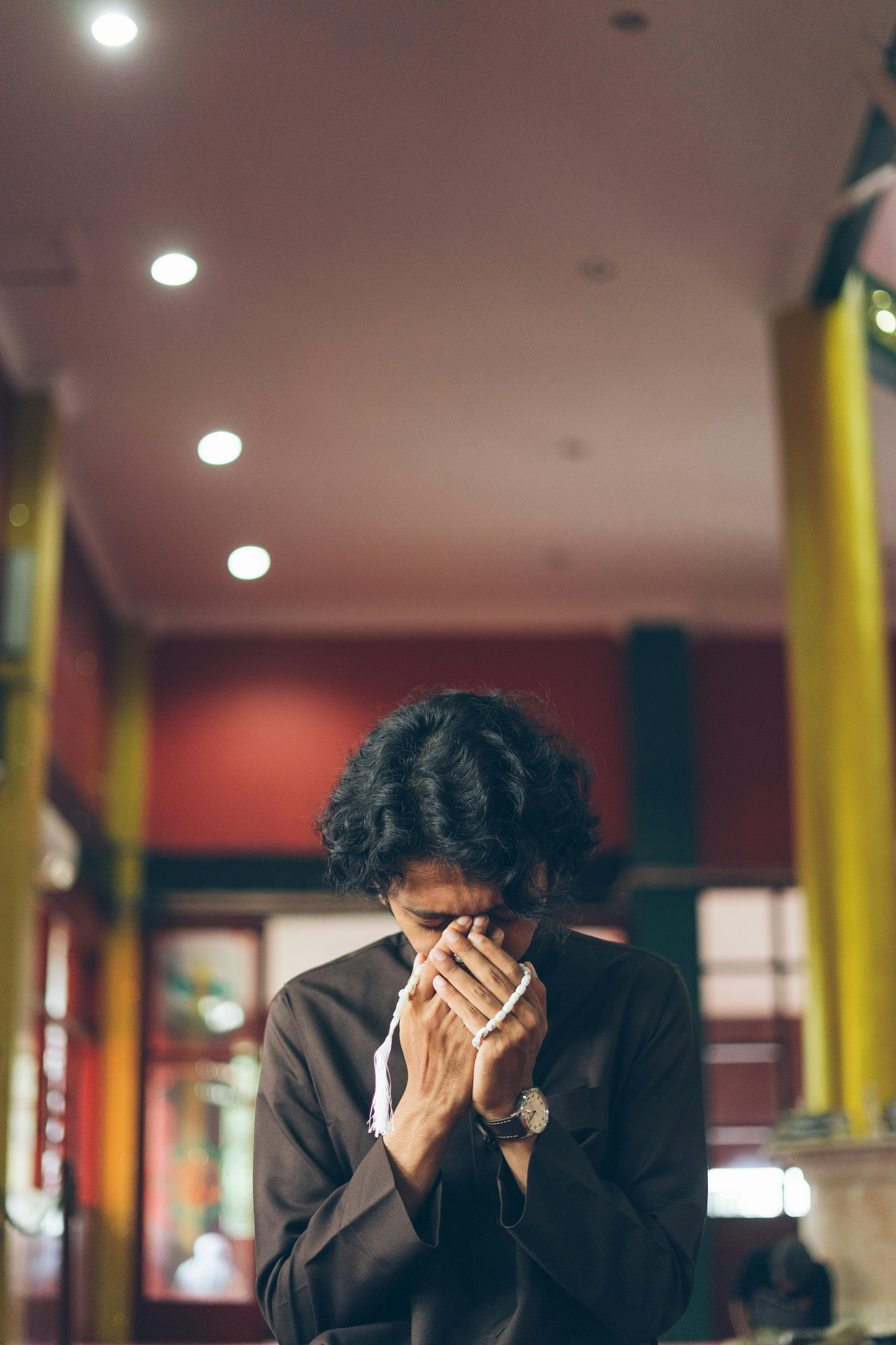 Gratis En mann i tradisjonelle klær ber inne i en bygning med fredelig belysning og dekor. Arkivbilde