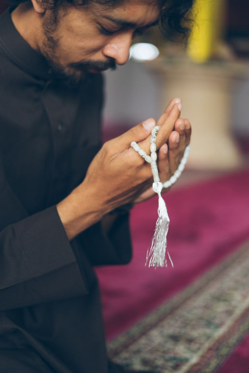 A man in traditional attire meditates with prayer beads in a peaceful mosque setting.