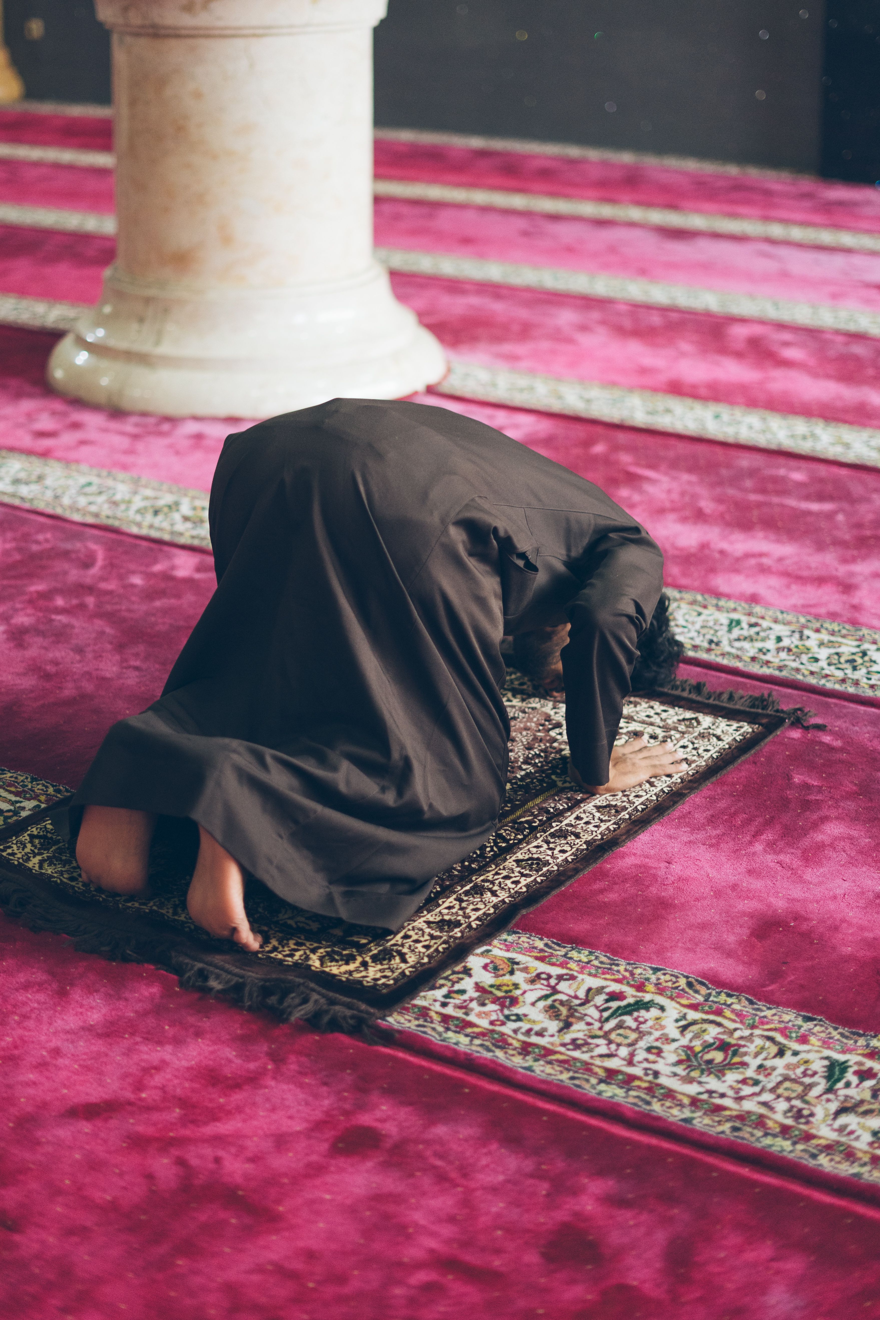 A person kneeling on a prayer rug in a mosque, performing Salah.