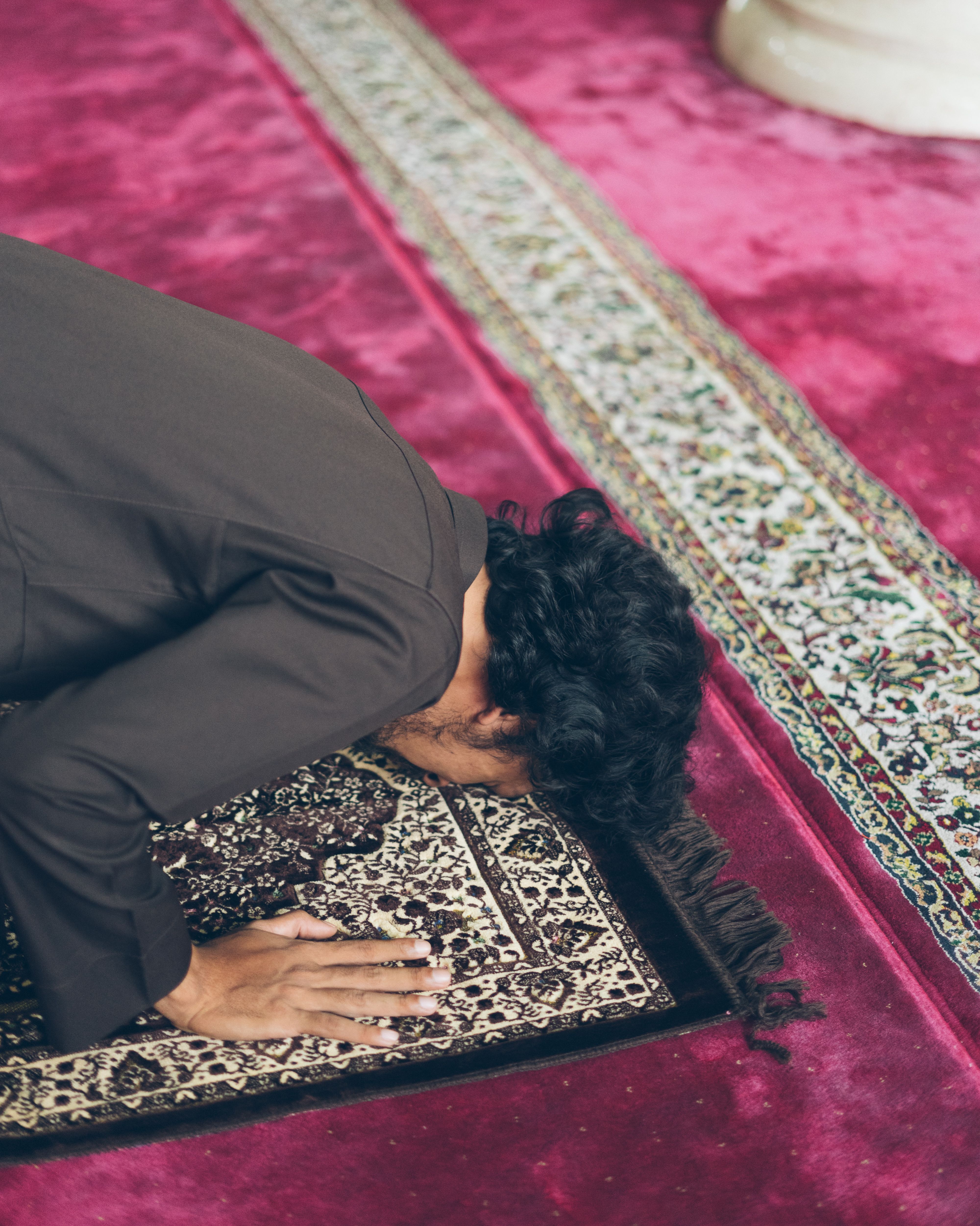 An adult man in prayer position on a patterned rug in a mosque, highlighting spiritual devotion.