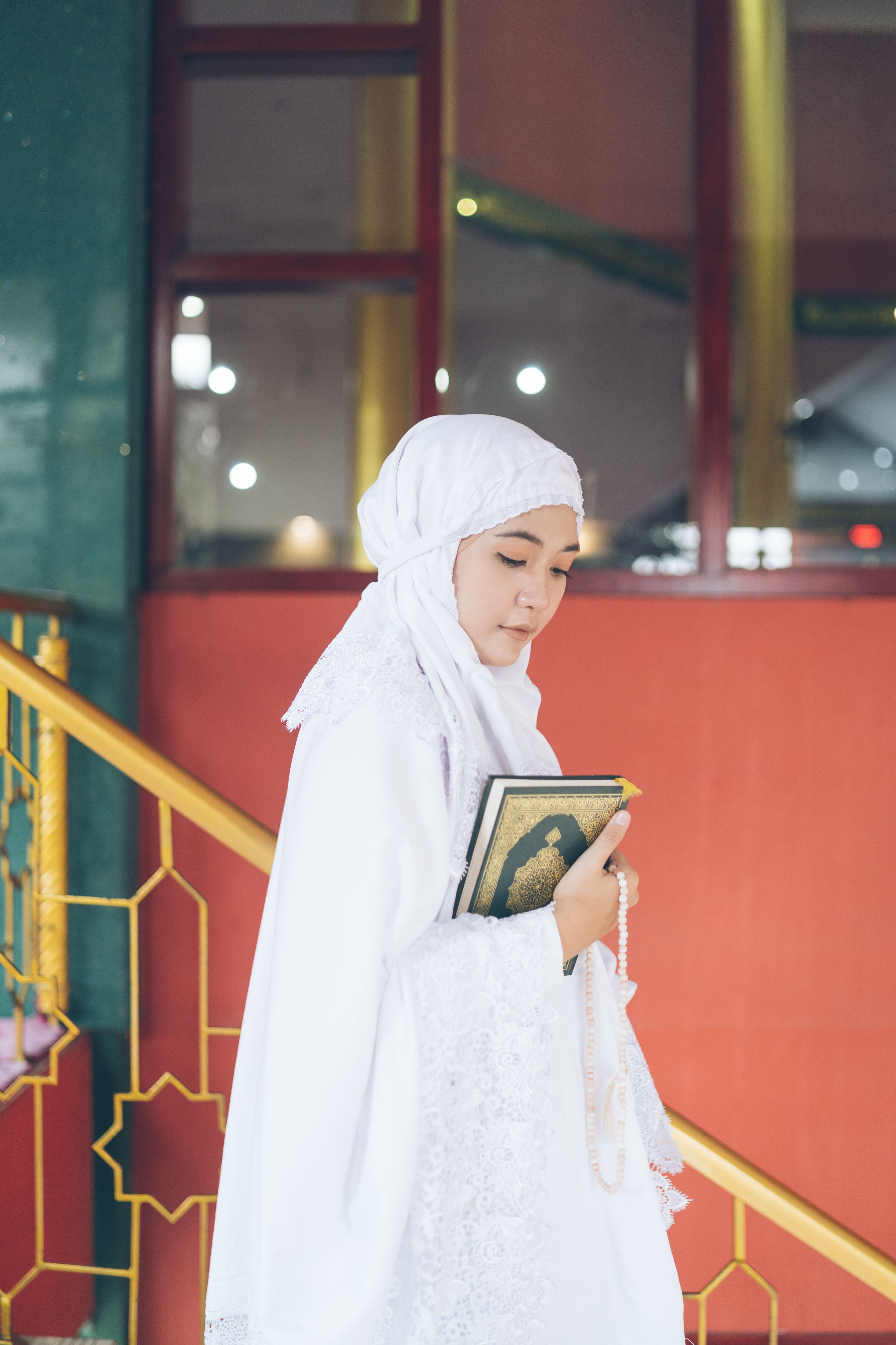 A woman in a white hijab holding a Quran stands inside a mosque, symbolizing faith and spirituality.