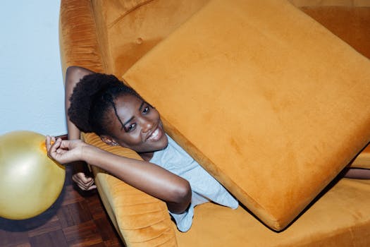 一个女人开玩笑地靠在室内的芥末色沙发上，旁边有一个金色的气球