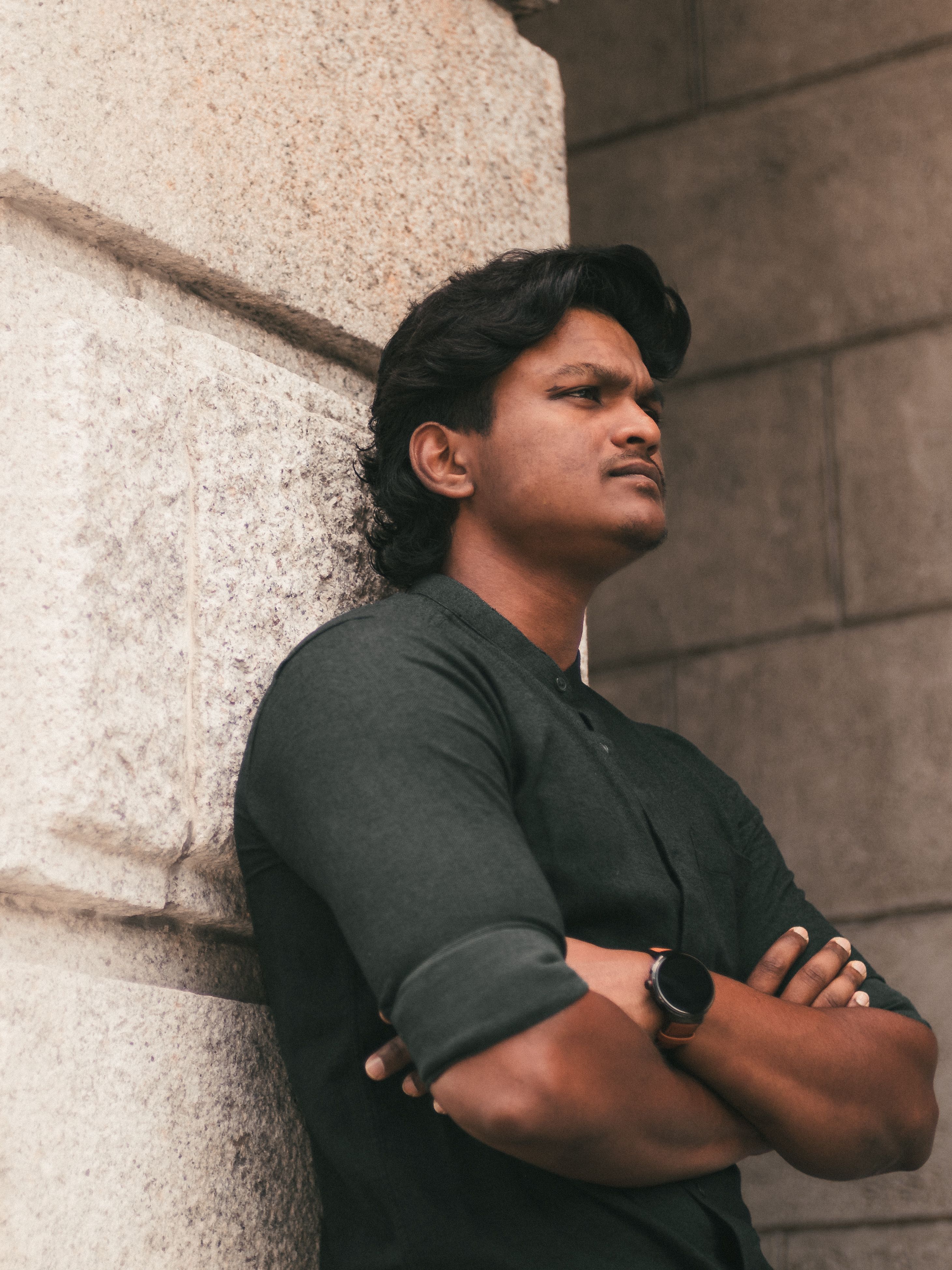 Portrait of a young man leaning against a stone wall in George Town, Malaysia, exuding confidence.