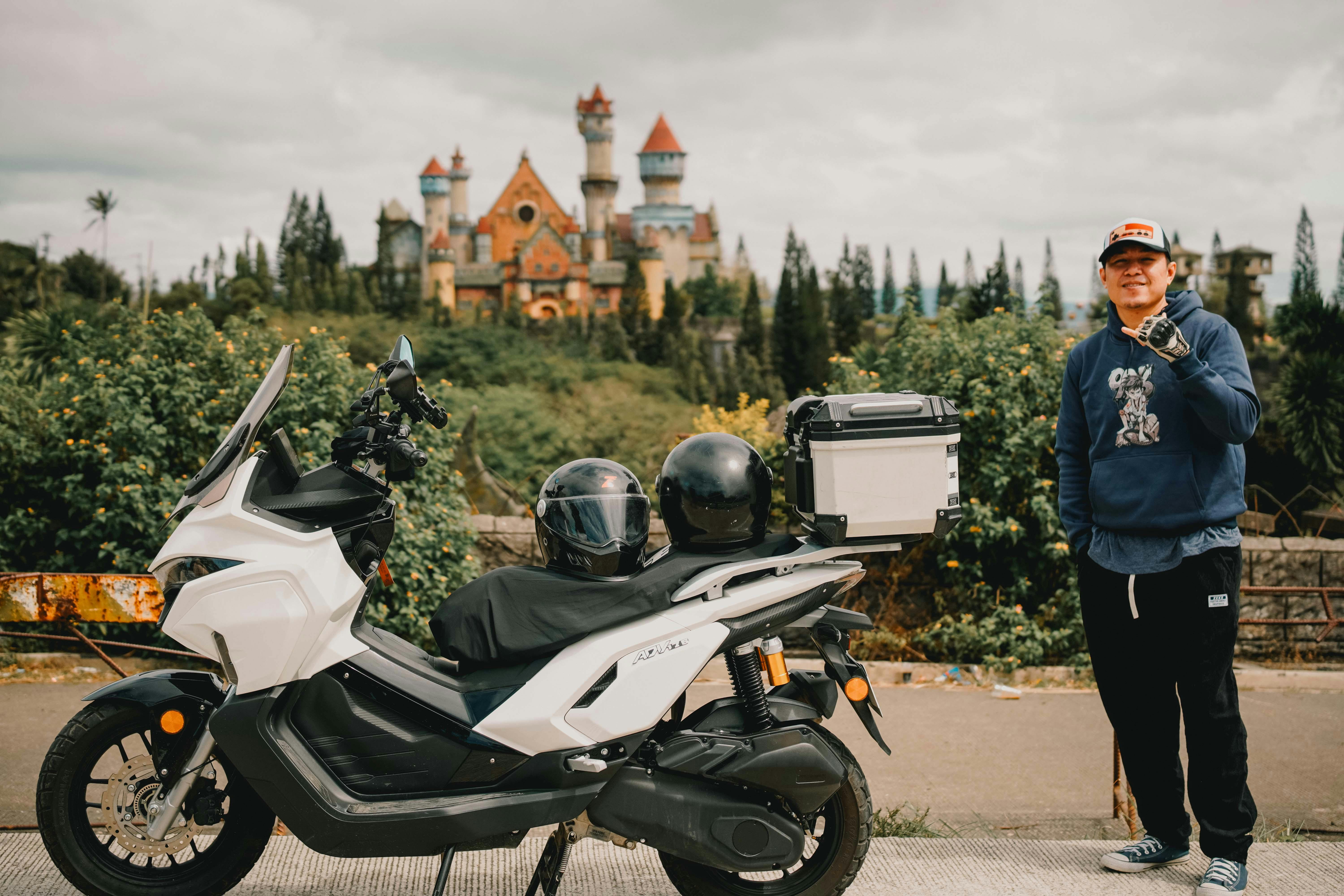 Ilmainen Mies seisoo moottoripyörän vieressä lähellä fantasialinnaa pilvisenä päivänä. Kuvapankkikuva