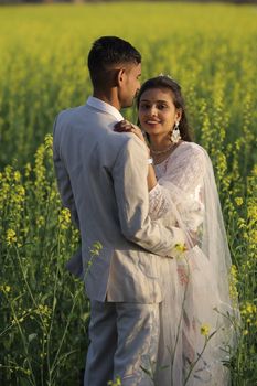 A loving couple in traditional attire shares a romantic moment in a lush mustard field. - Fotografer Sidoarjo