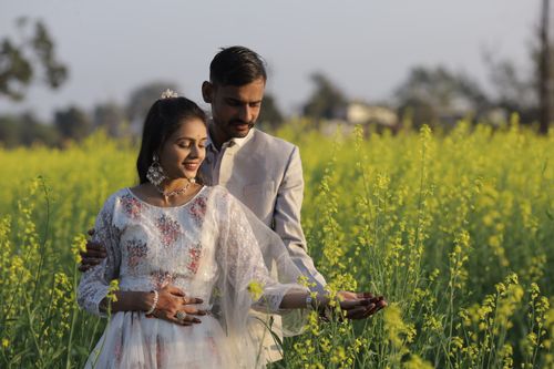 Free A loving couple in traditional attire embracing amidst yellow mustard flowers in a serene Indian field. Stock Photo