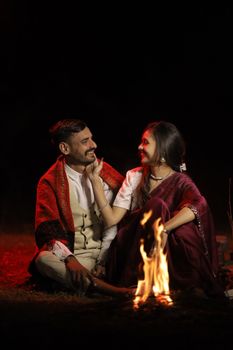 An Indian couple sharing a romantic moment by the campfire, dressed in traditional attire under the night sky. - Fotografer Sidoarjo