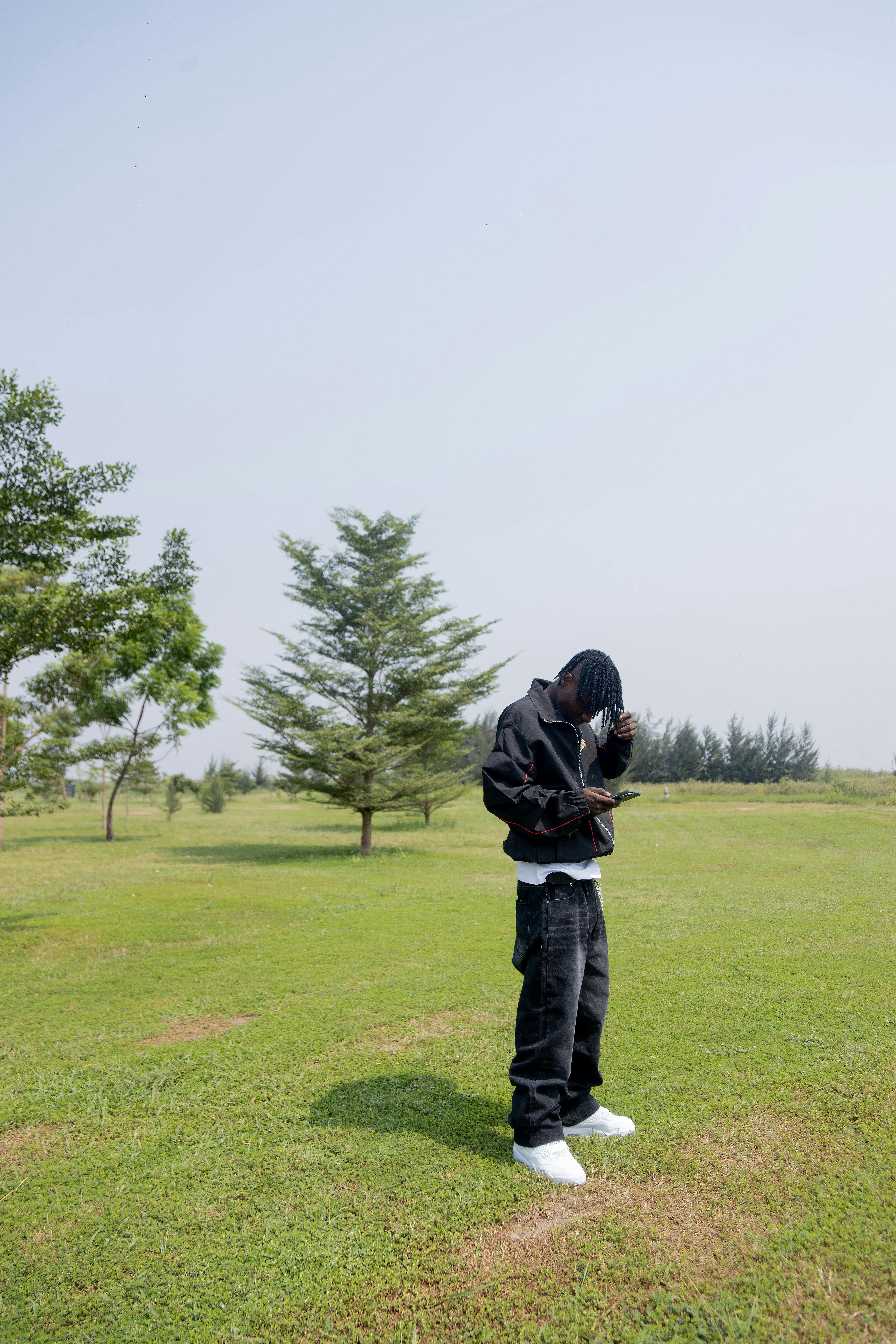 Ücretsiz Parkta, yeşil ağaçlarla çevrili bir alanda, siyah ceket ve kot pantolon giymiş genç bir adam. Stok Fotoğraflar