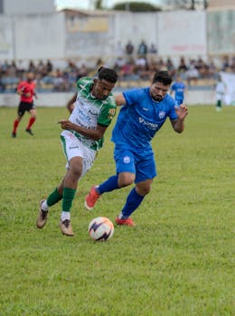 Two soccer players in green and blue jerseys compete during a match on a grassy field.