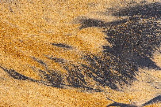 Close-up of ilmenite and yellow sand forming natural abstract patterns on a beach.