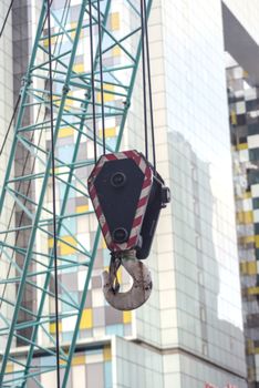 Close-up of a tower crane's hook in a city construction site, high-rise buildings in the background.