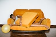 一位快乐的女士正舒适地躺在橙色沙发上放松，房间里飘着气球