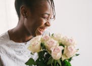 微笑的女人在室内享受着一束粉红色的玫瑰，散发着幸福和温暖