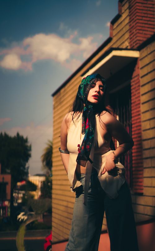 Free Fashionable woman poses outdoors in sunlight, wearing a scarf and vintage style outfit. Stock Photo