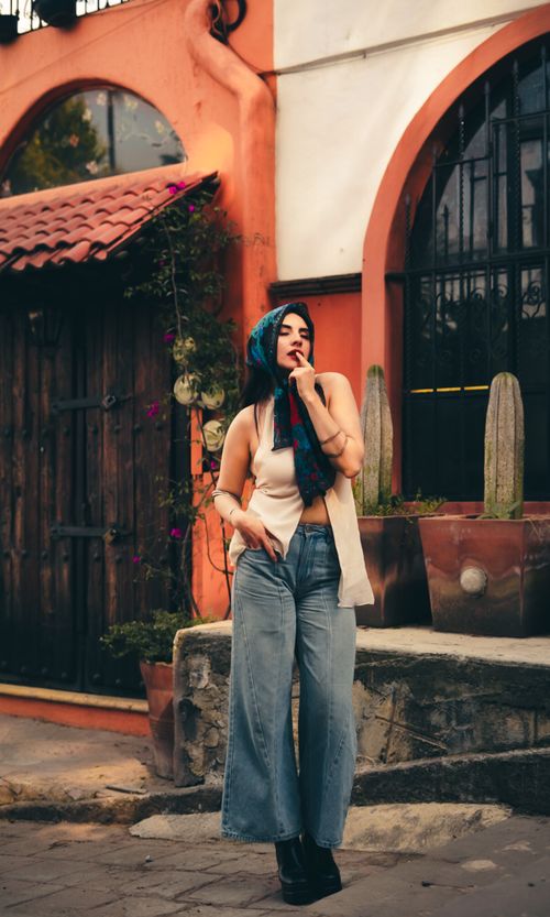 Free Stylish woman with scarf posing by rustic house, exuding modern fashion vibes. Stock Photo