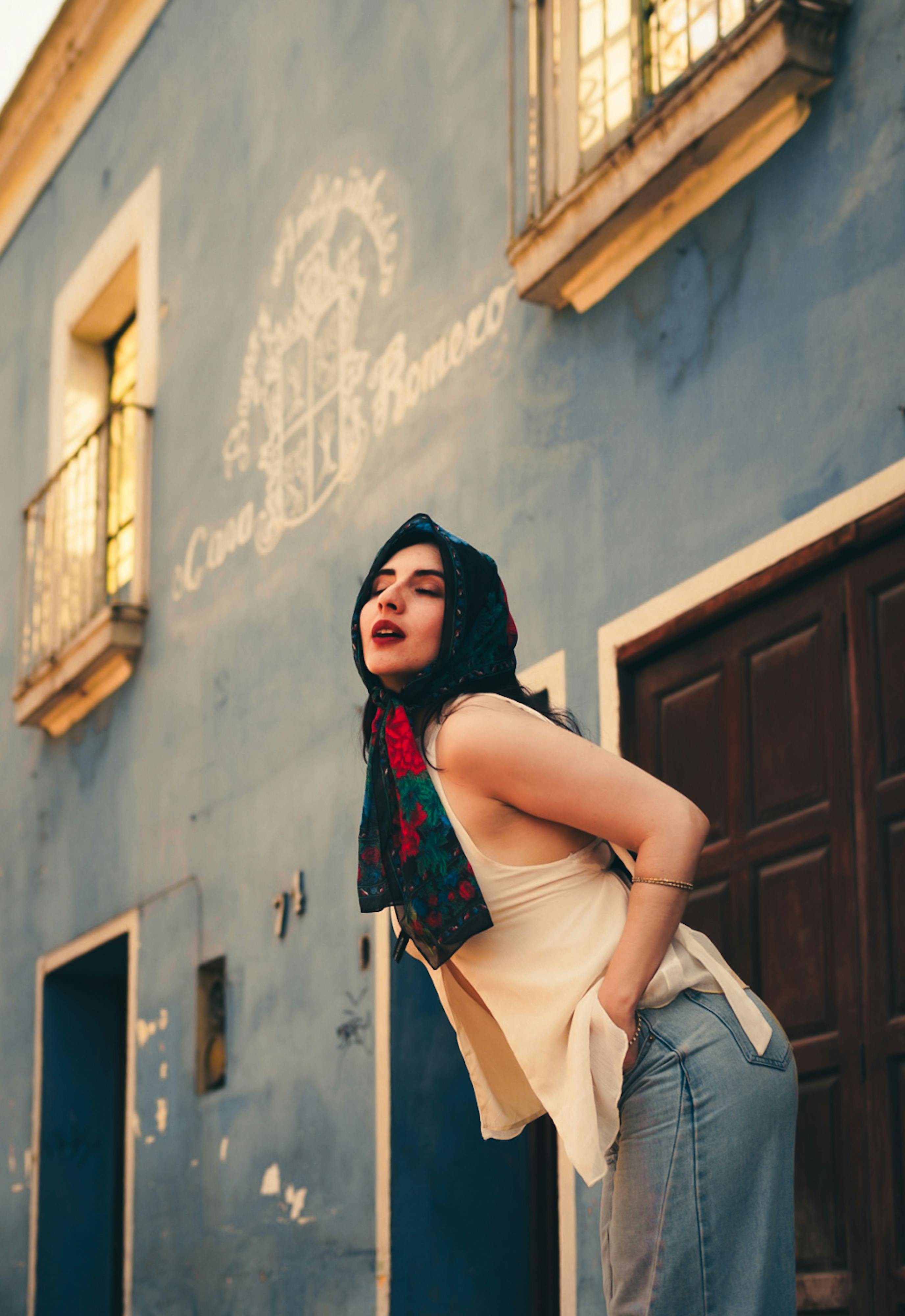 Zadarmo Módna žena so šatkou pózuje pri rustikálnej modrej budove s umeleckou atmosférou. Fotka z fotobanky