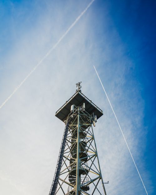 Free Metal tower set against a clear blue sky with criss-crossing vapor trails captured in golden hour. Stock Photo
