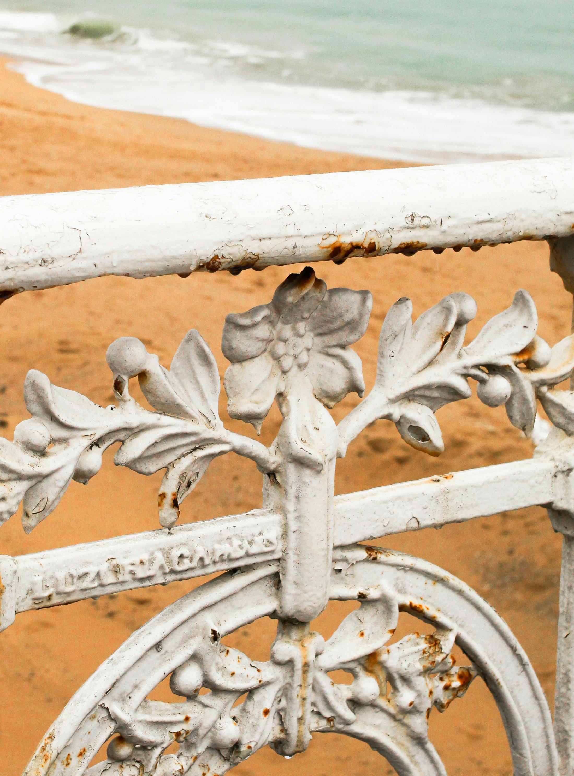 Gratis Nærbillede af et rustent ornamentalt jernrækværk med strand i baggrunden. Lagerfoto