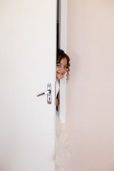 A bride playfully peeks through a door, capturing the excitement before her wedding ceremony.