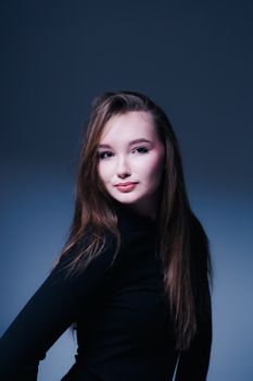 Studio portrait of a woman with long hair, wearing a black outfit, against a blue background.