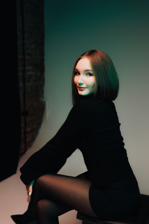 Free A stylish portrait of a young woman in a black outfit, sitting in studio lighting. Stock Photo