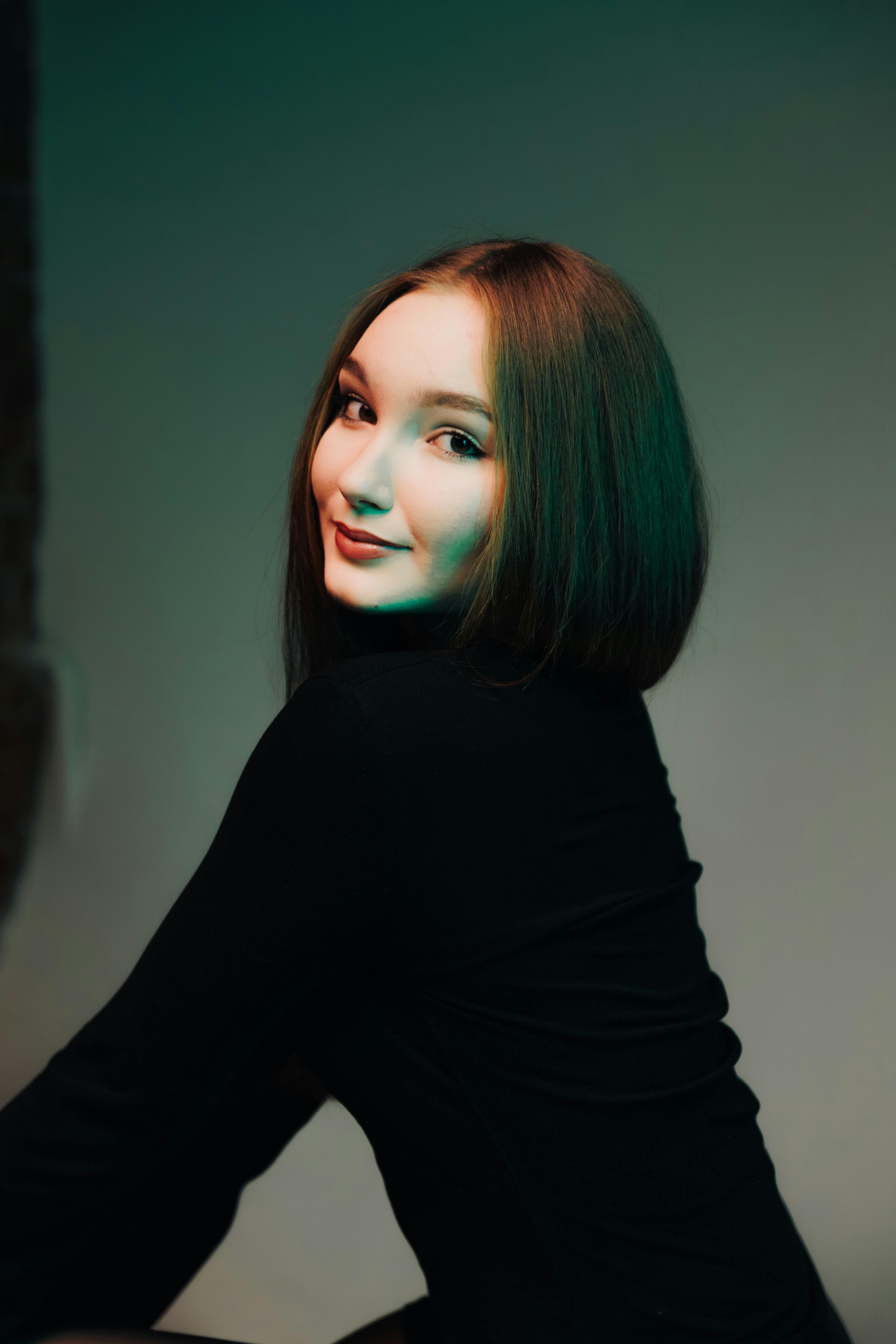 Gratis En ung kvinde poserer selvsikkert med en blød, kunstnerisk belysning i baggrunden. Lagerfoto