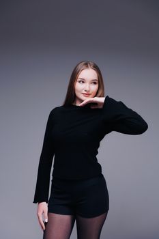 Stylish young woman in a black outfit posing confidently in a studio setting.