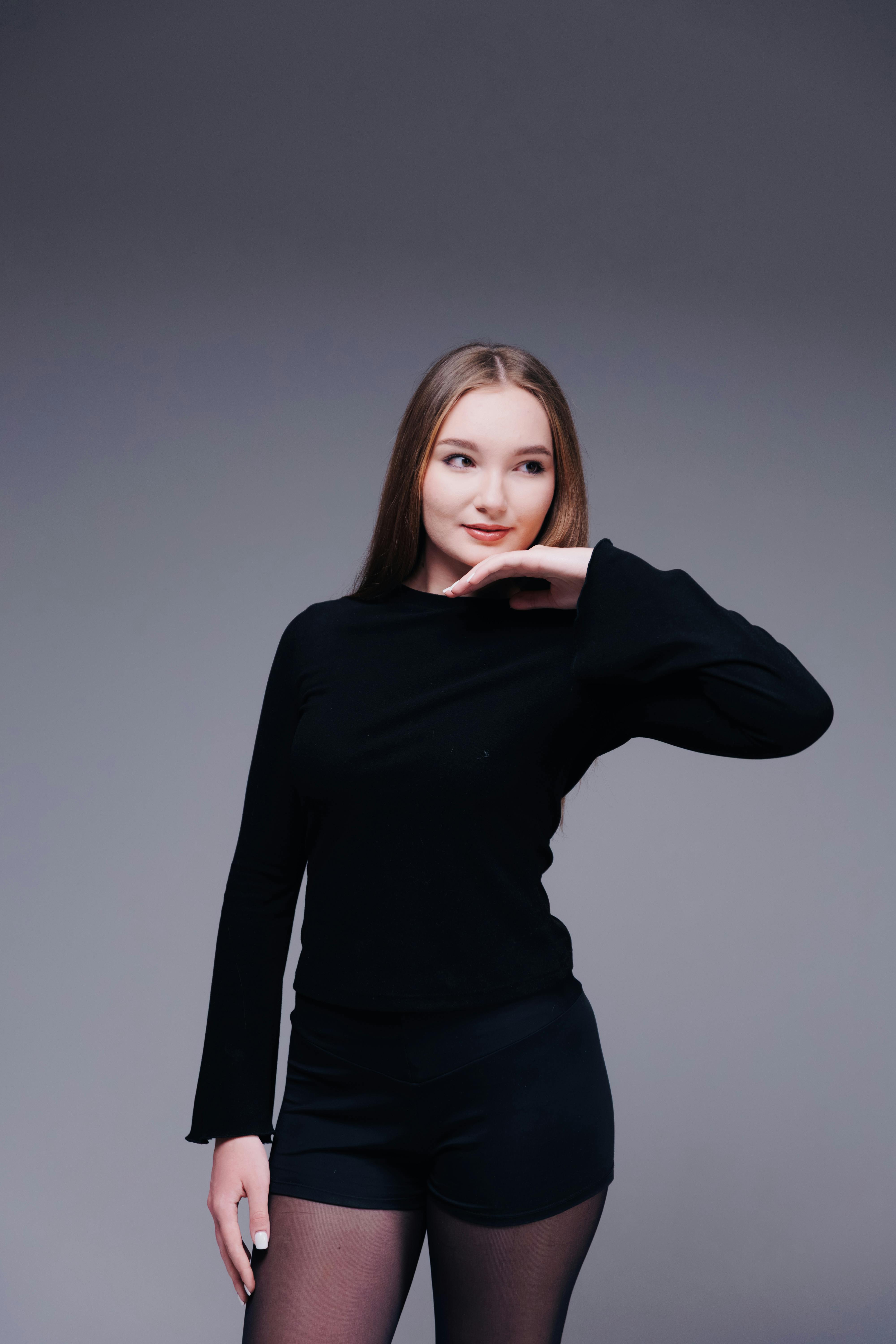 Bezpłatne Stylowa młoda kobieta w czarnym stroju pozuje pewnie w studiu. Zdjęcie z galerii