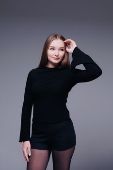 A confident young woman in a chic black outfit posing against a neutral studio background.