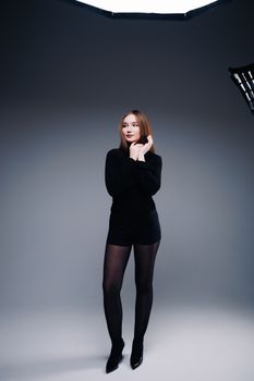 Studio portrait of a woman in a stylish black outfit standing gracefully against a gray background.