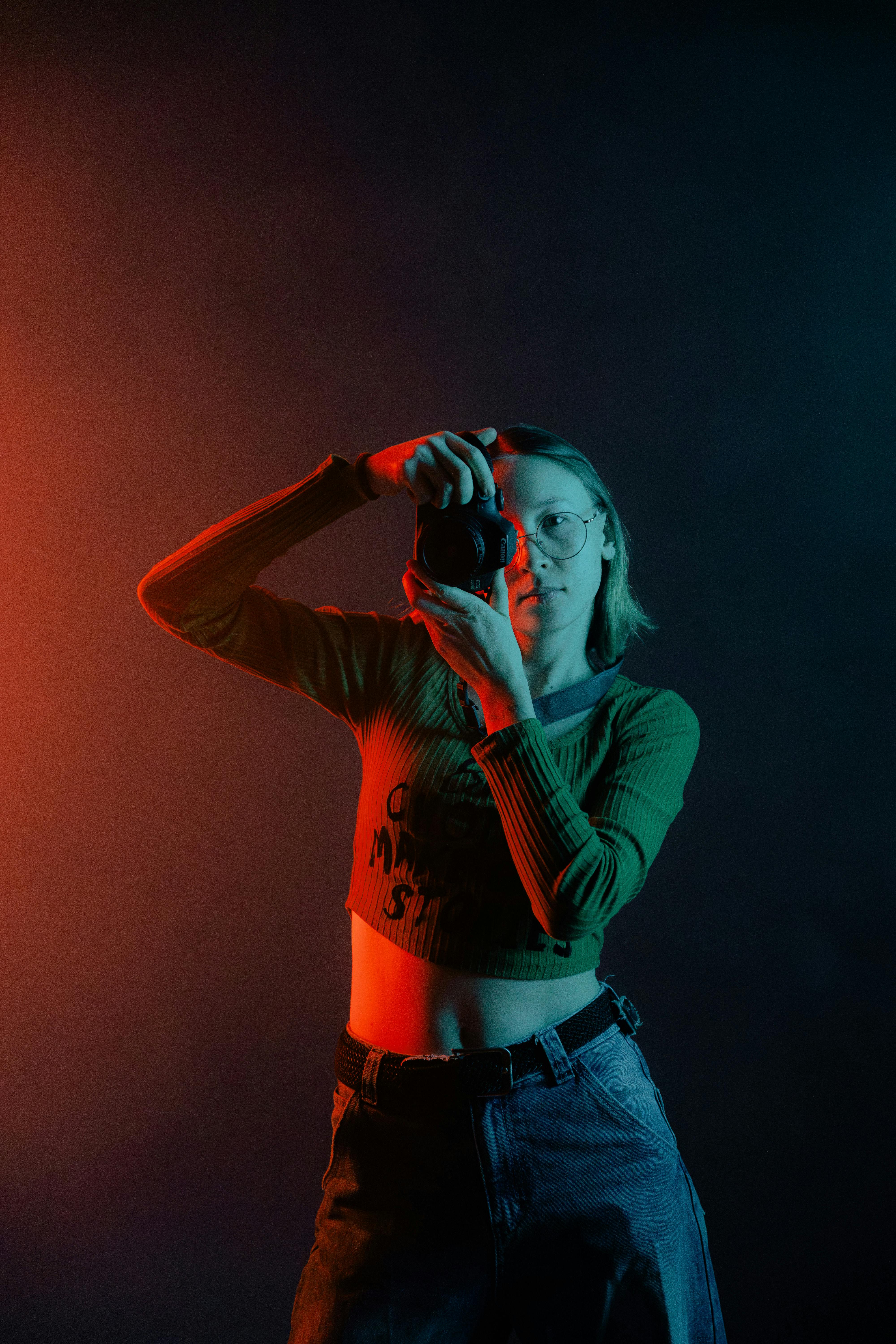 Bezpłatne Artystyczny portret kobiety fotografki w żywym oświetleniu z aparatem. Zdjęcie z galerii