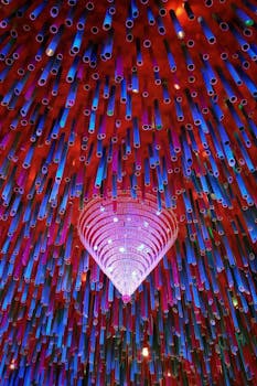 Colorful ceiling with hanging tubes and chandelier, creating an abstract pattern.