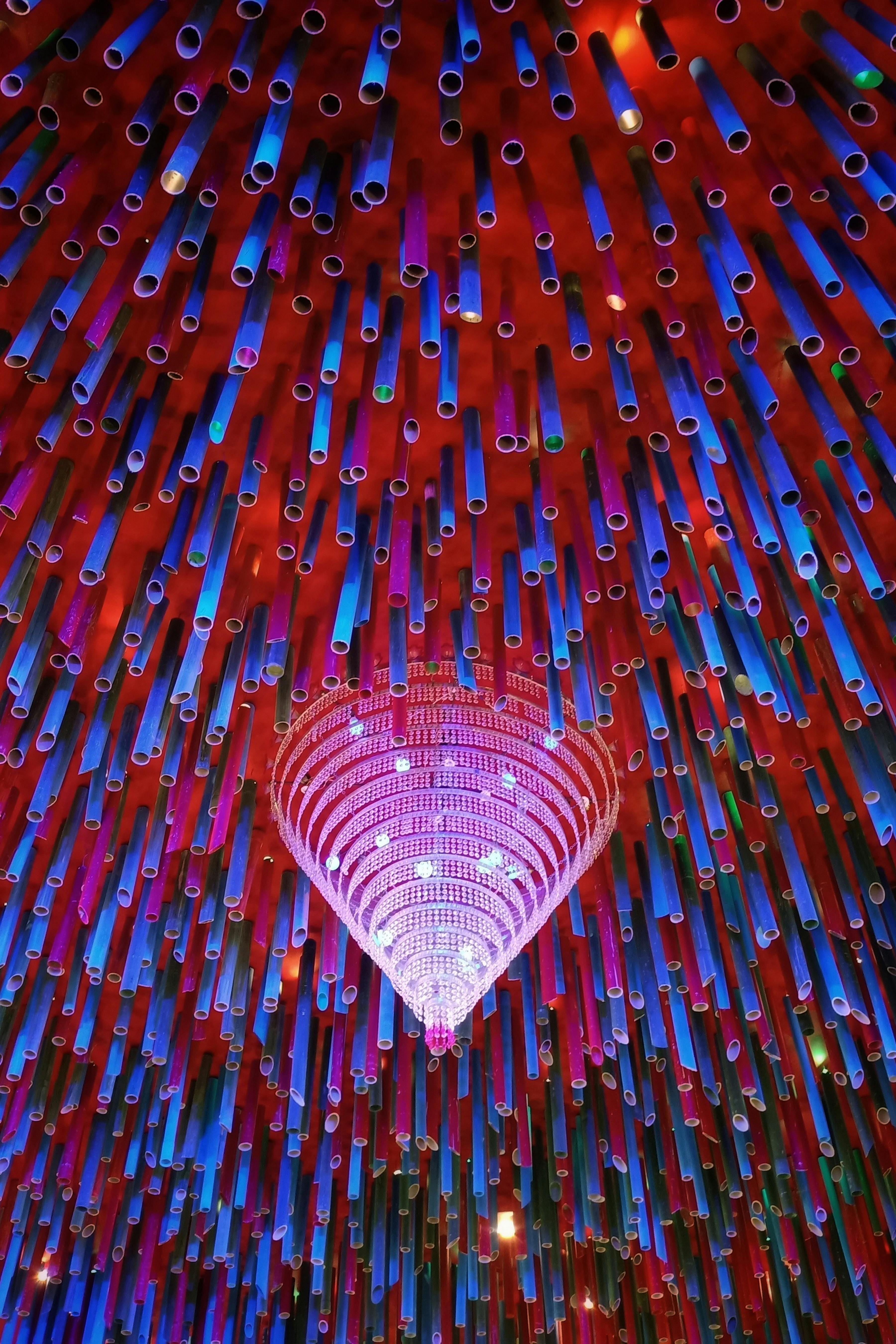 Gratis Langit-langit berwarna-warni dengan pipa-pipa gantung dan lampu gantung, menciptakan pola abstrak. Foto Stok