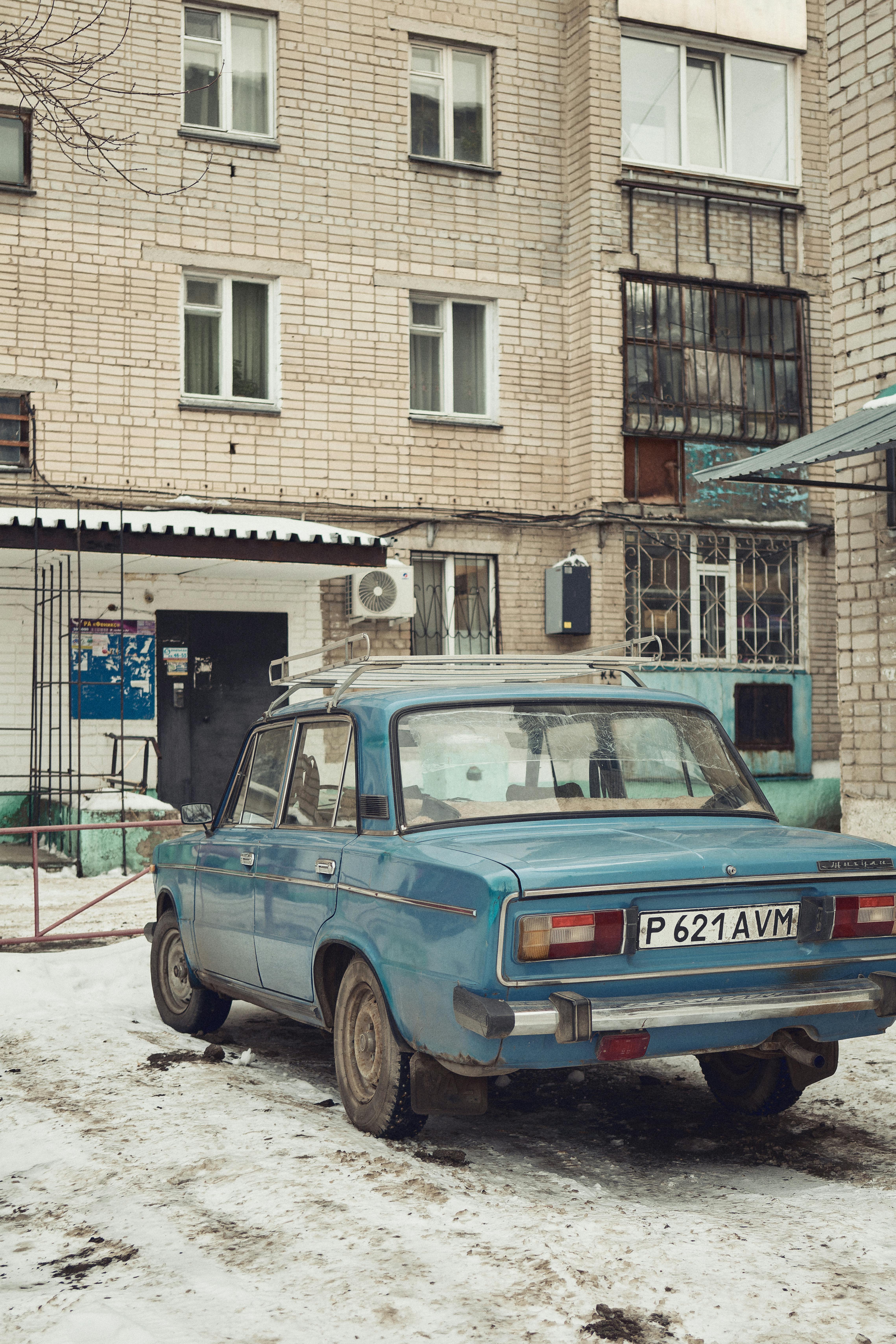 Gratis Una classica auto blu parcheggiata davanti a un condominio urbano durante l'inverno. Foto a disposizione